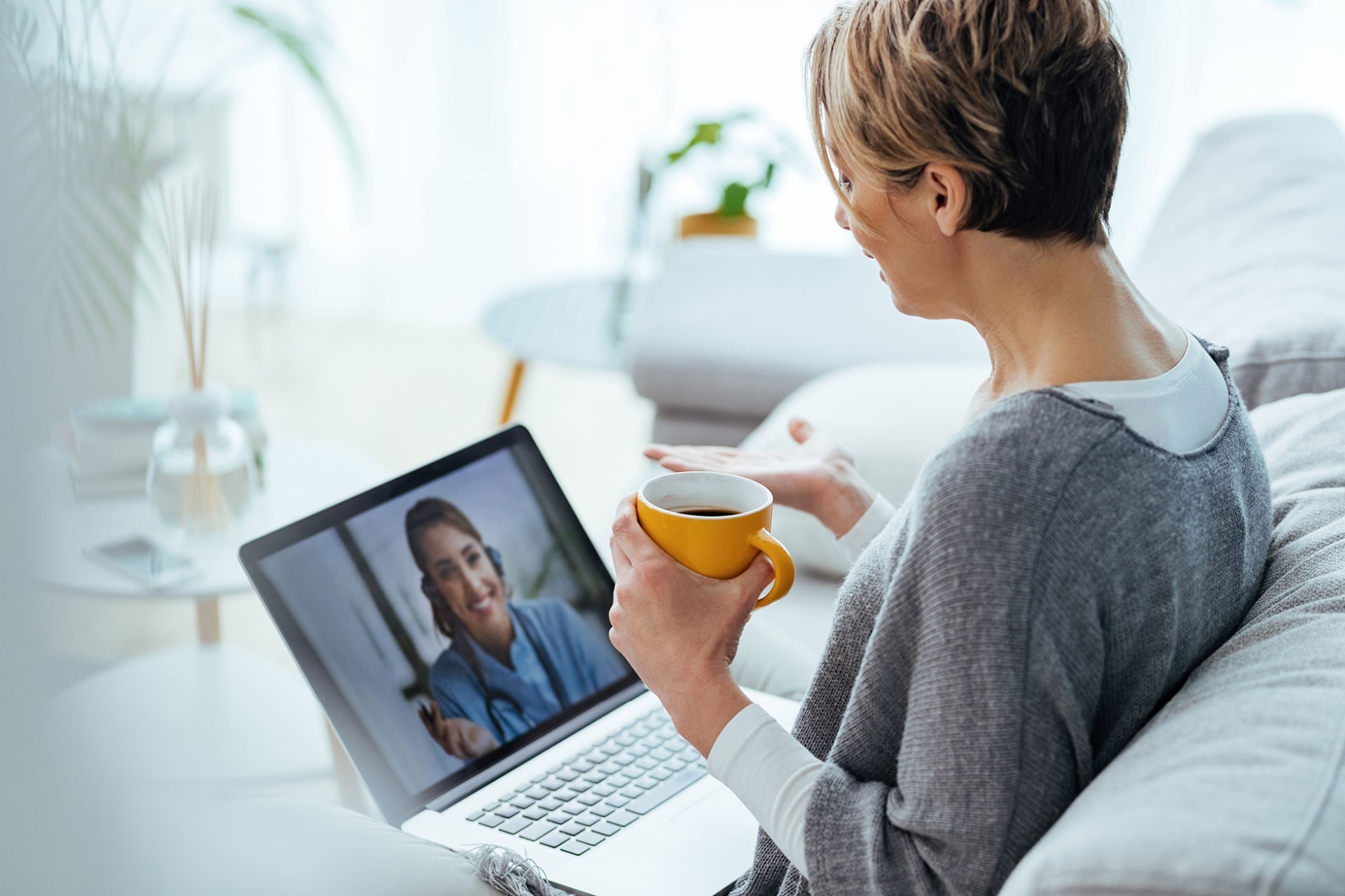 Lady with a coffee, talking to a Doctor on a laptop