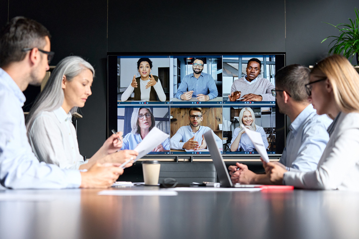 A group of 4 people talking to another group of people on video chat, having a virtual meeting to discuss their plans